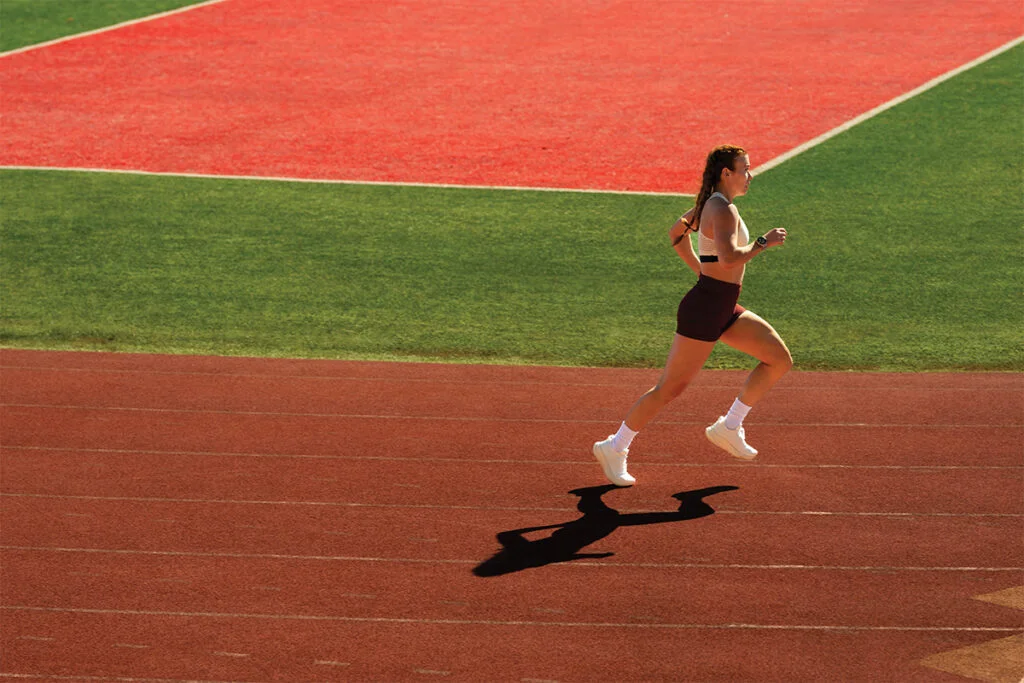 A woman wearing Garmin Forerunner 970 and HRM 600 runs on a track.