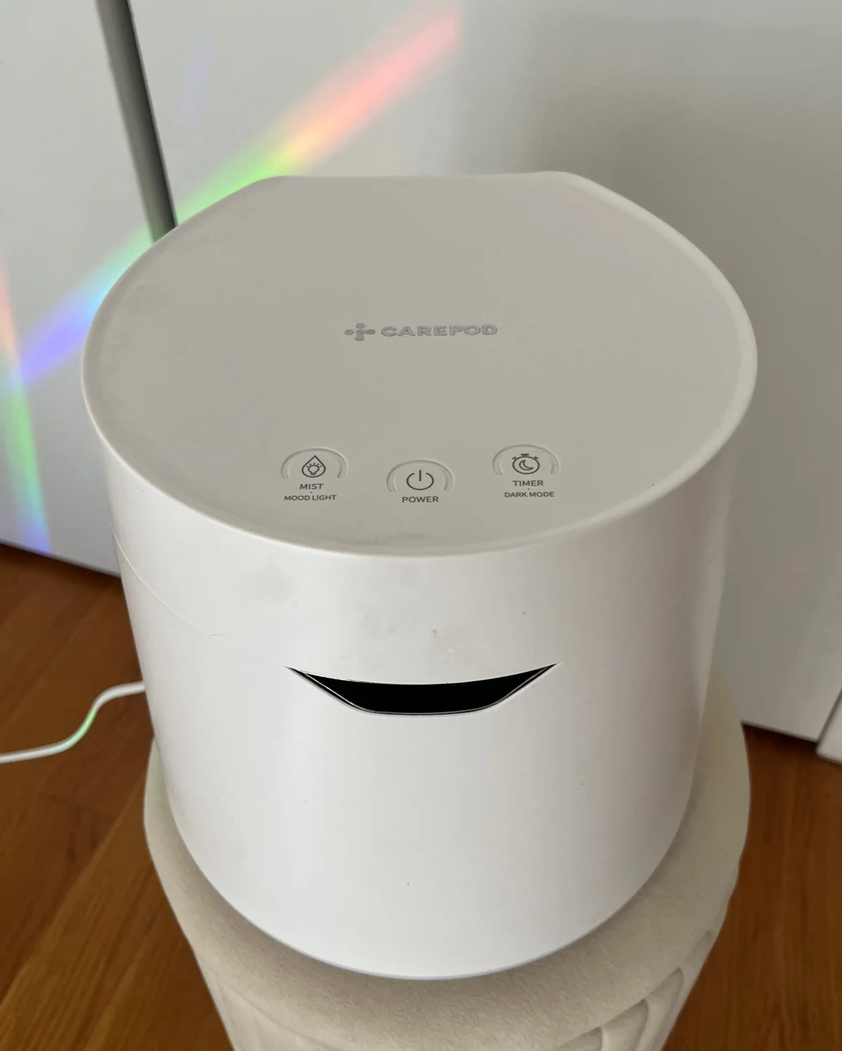 White essential oil diffuser with control buttons on top, placed on a beige pouf.