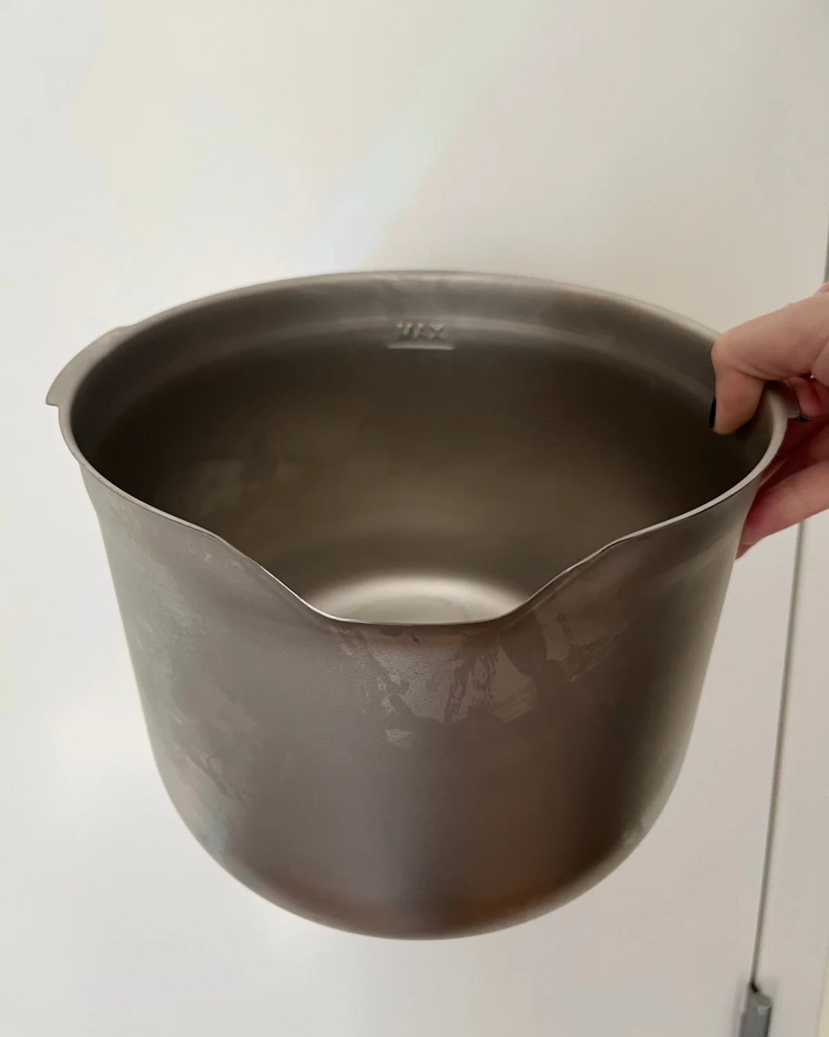 Metal mixing bowl being held with a slightly angled opening and smooth surface.